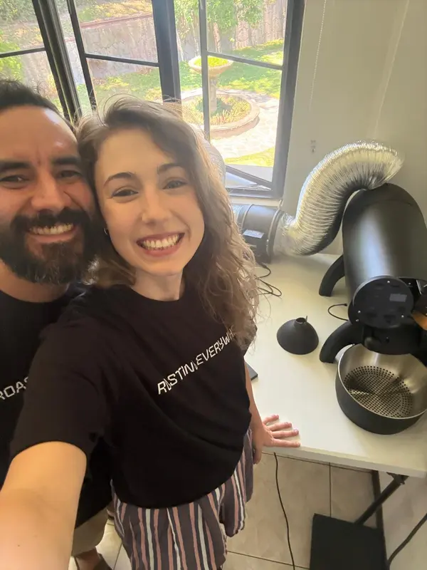 Miguel and Joanna laughing together in bright window light at the roaster.